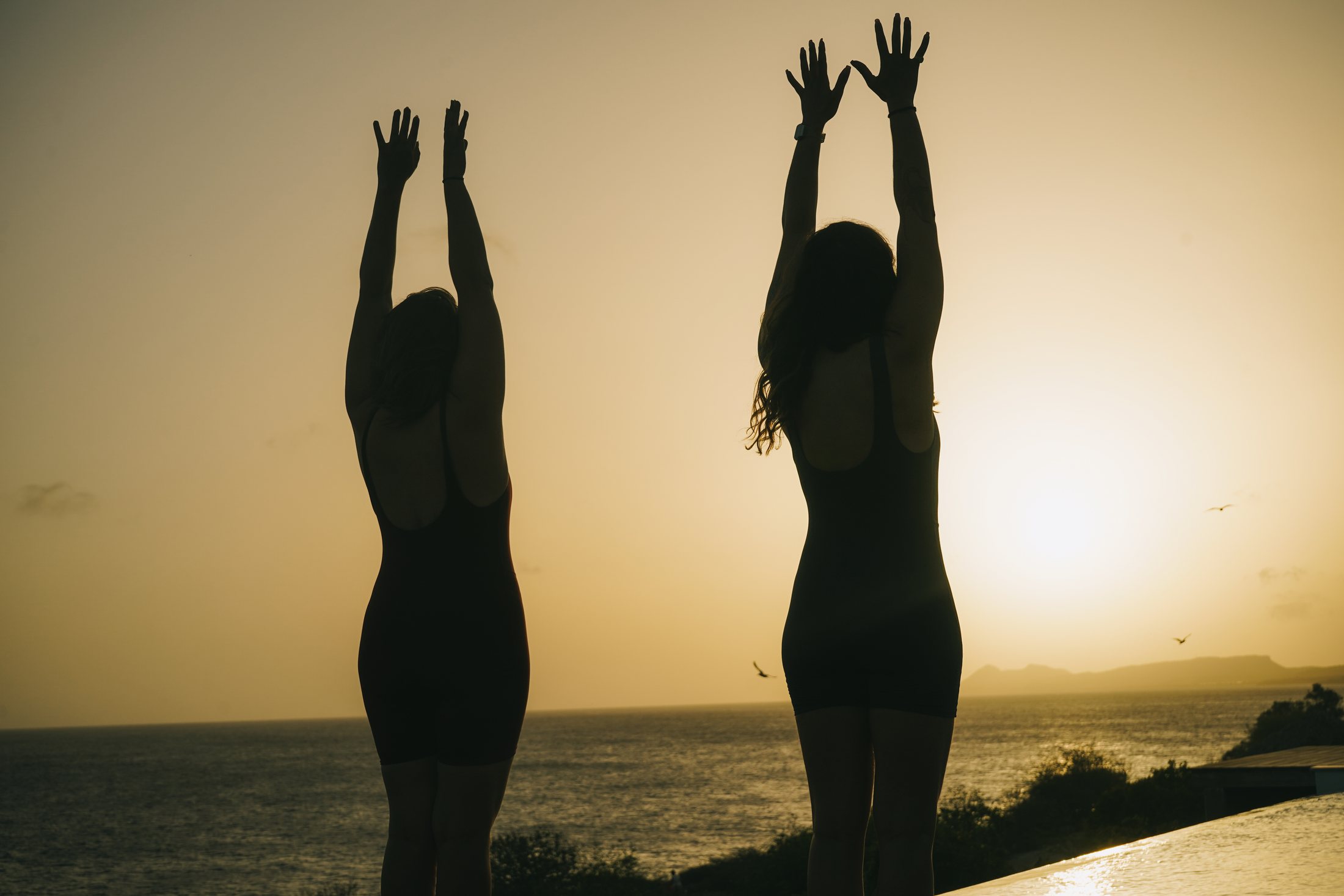 Two women practising sunset yoga by the ocean at a Bonaire retreat